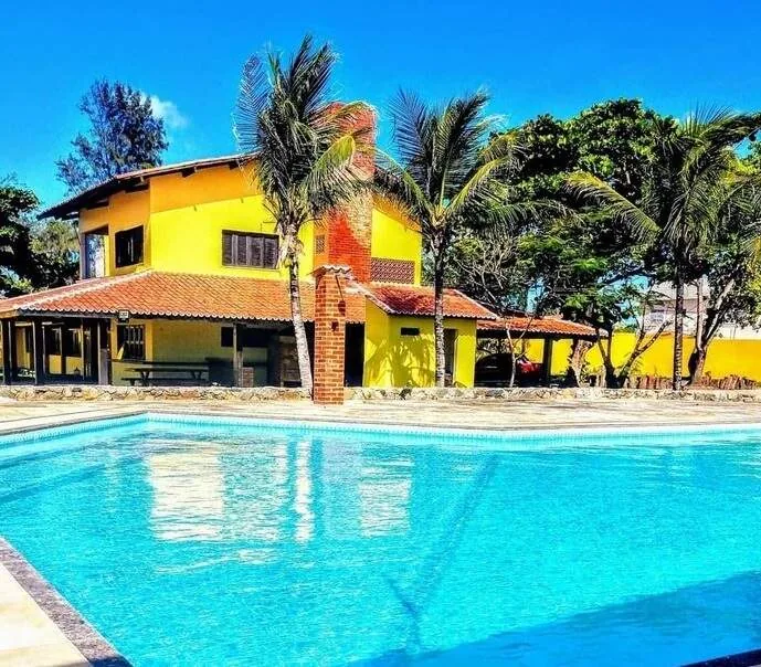 Casa amarela com piscina e palmeiras em uma unidade da clínica de recuperação do Grupo Flor de Liz